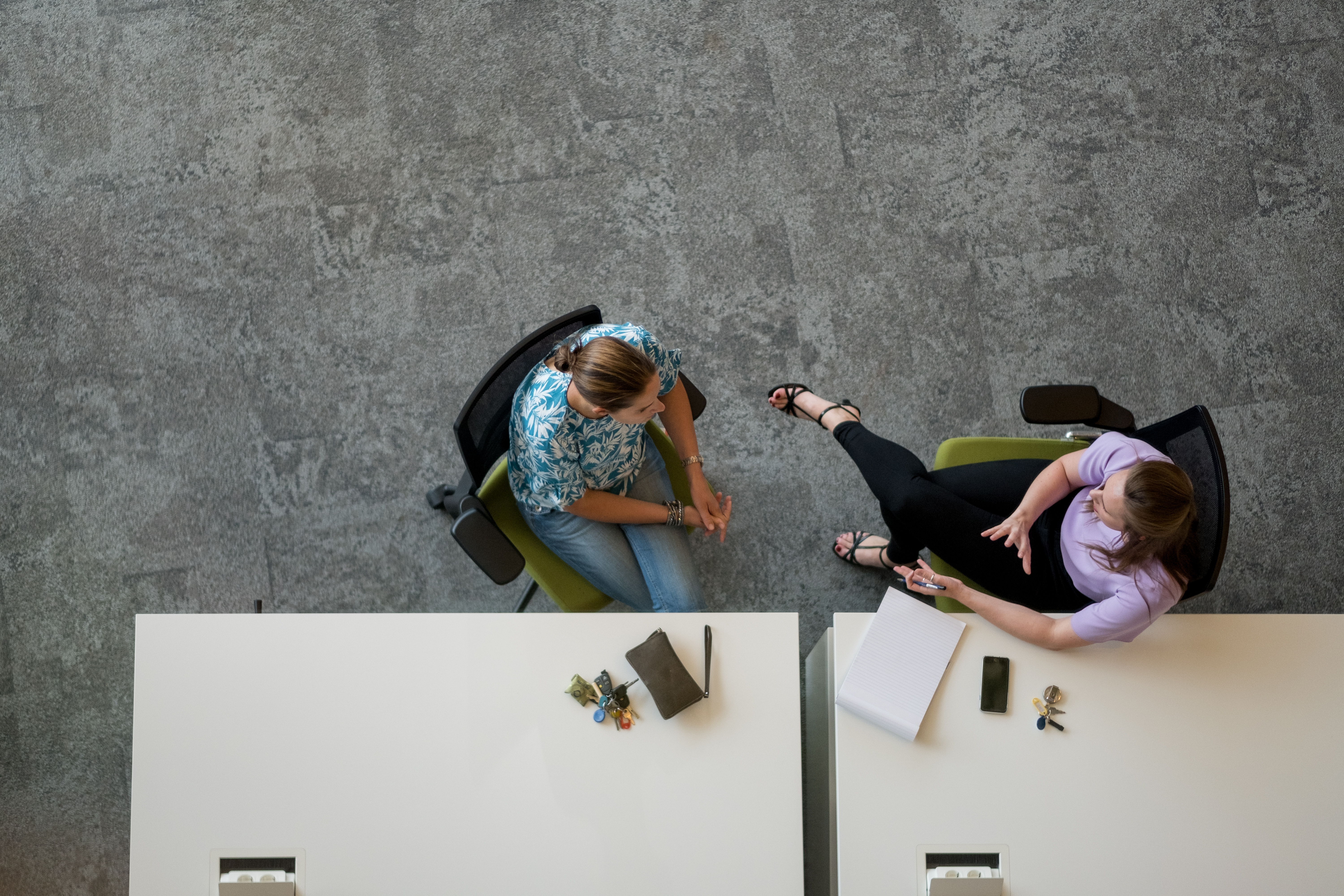 Foto van bovenaf genomen van 2 medewerkers in gesprek aan een bureau